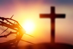Crown of thorns of Jesus Christ against wooden catholic cross at sunset background
