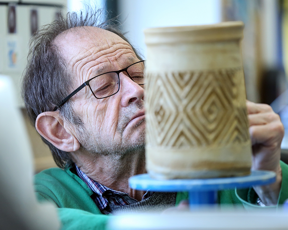An elderly man carves a complicated pattern into a ceramic vase