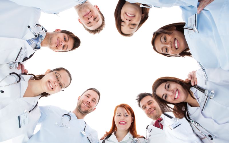 Large diverse multiethnic medical team standing grouped in a circle all looking down at the camera and smiling isolated on white with central copyspace