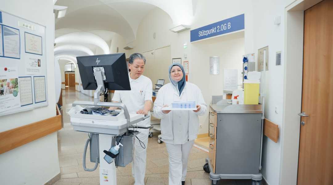 Frater Johannes mit Pflegekraft im Gang auf einer Station mit Visitenwagen