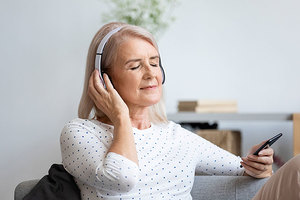 Das Bild zeigt eine Frau auf der Couch, die über Kopfhörer Musik hört.