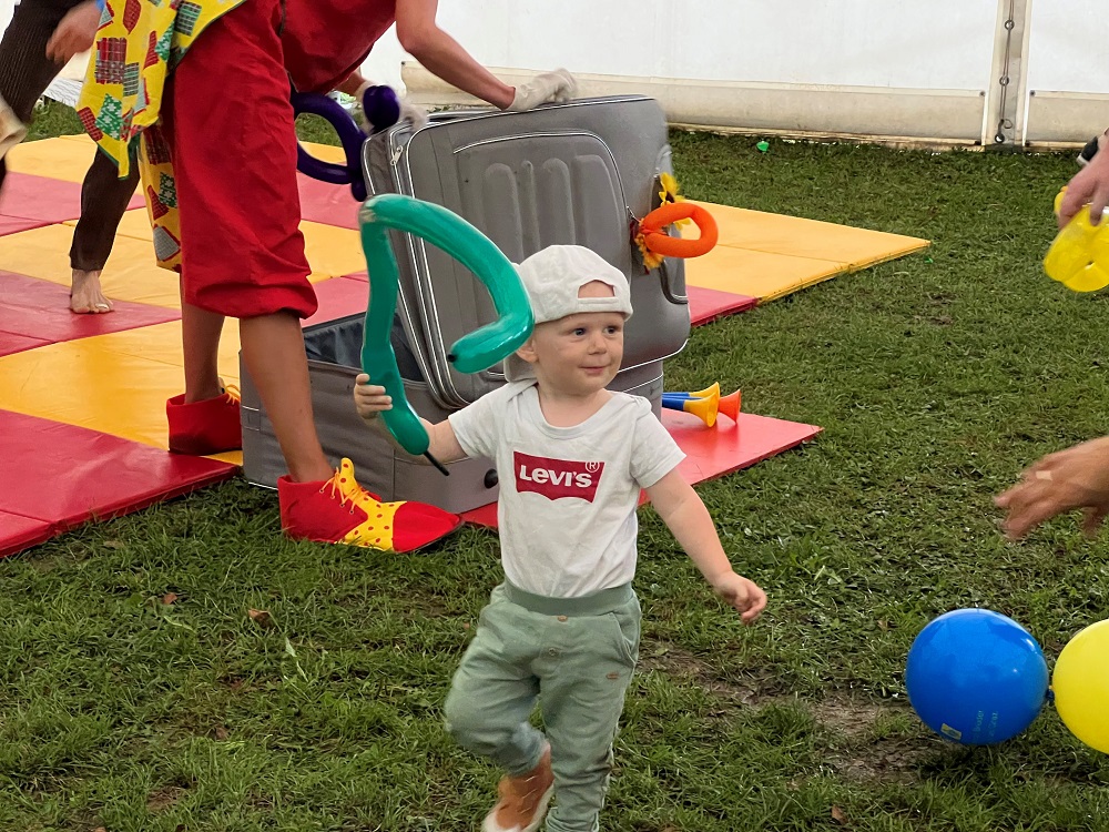Das Bild zeigt ein kleines Kind in der Zirkusmanege mit einem Luftballon in der Hand