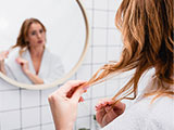 Das Bild zeigt eine Frau, die ihre Haare im Spiegel betrachtet.