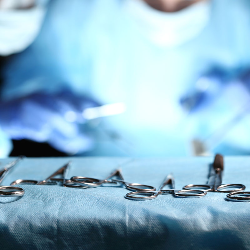 Surgical tools lying on table wile group of surgeons at background operating patient in surgical theatre. Steel medical instruments ready to be used. Surgery and emergency concept