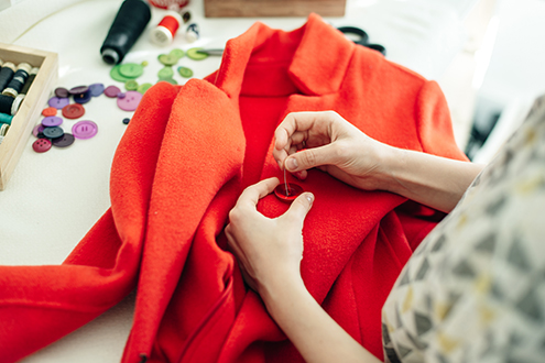 a seamstress sews a button on a red coat.