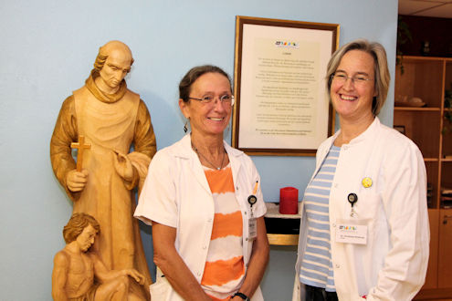 Mitarbeiterinnen vor dem Leitbild und der Johannnes von Gott- Statue