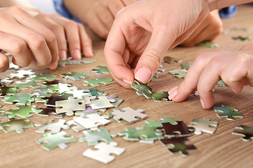 Female hands assembling puzzle on wooden table, closeup