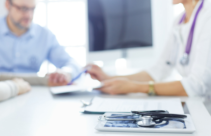 Doctor in clinic asking senior woman in wheelchair for a signature.