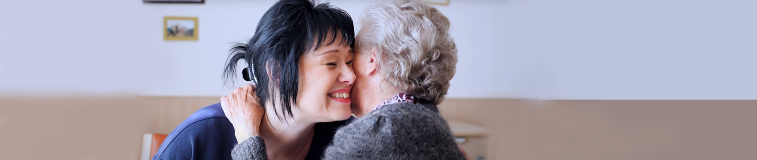 Eine Pflegerin und eine Seniorin umarmen sich.