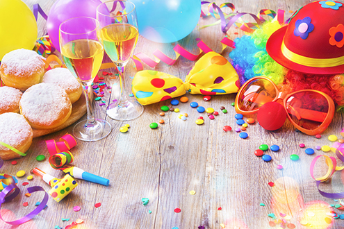 Colorful carnival or party background with donuts, balloons, streamers and confetti and funny face formed from wig, nose and glasses on rustic wooden planks with copy space
