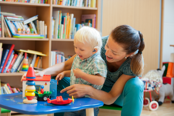 Auf dem Foto sieht man eine Mutter mit ihrem hörbeeinträchtigten Kind spielen.