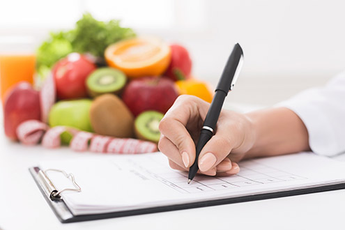 Doctor writing prescription for patient, making diet plan at workplace with fresh fruits, panorama