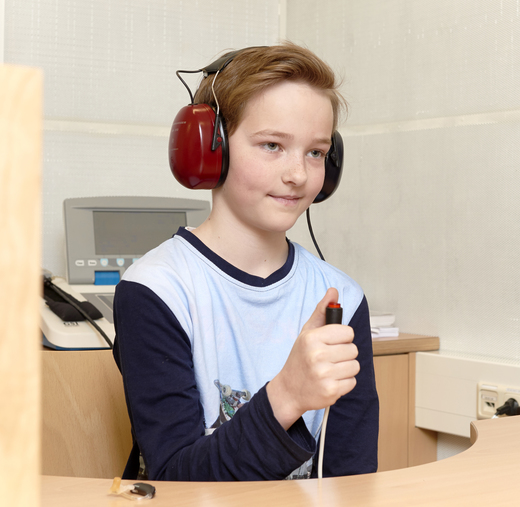 Das Foto zeigt einen Jungen mit Kopfhörern, der gerade einen Hörtest macht.