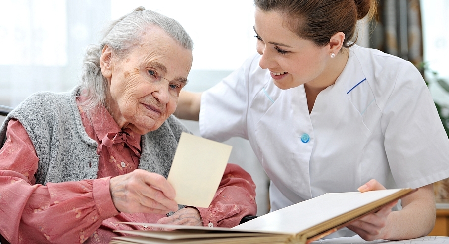 Senior woman and nurse looking together at album with old photographs