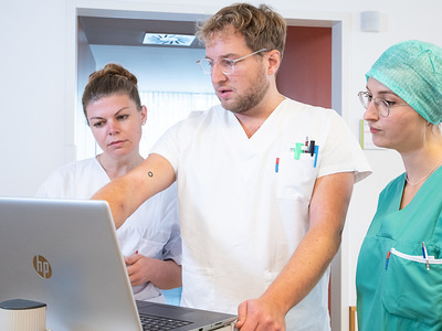 Das Foto zeigt drei Pflegepersonen vor einem Laptop, die gerade etwas besprechen.