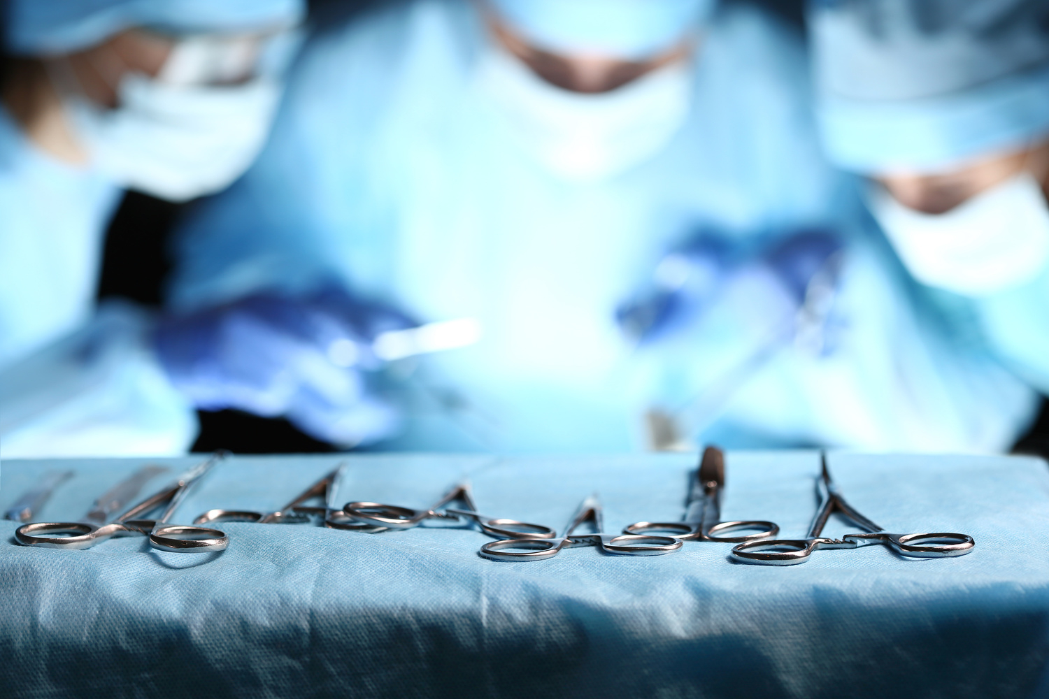 Surgical tools lying on table wile group of surgeons at background operating patient in surgical theatre. Steel medical instruments ready to be used. Surgery and emergency concept