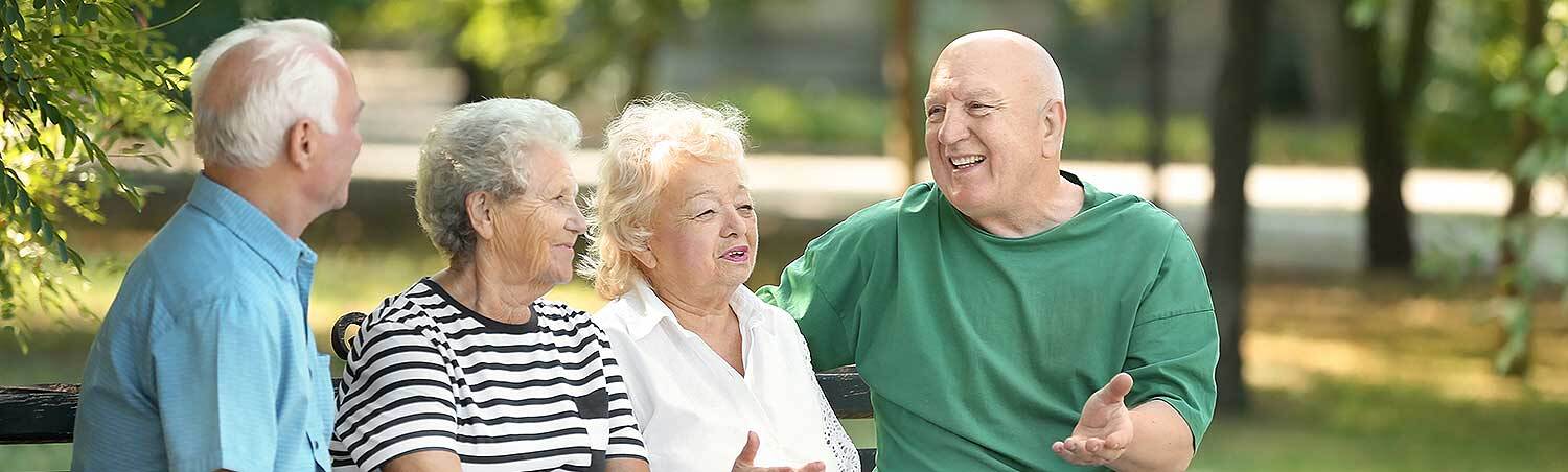 Das Bild zeigt ältere Menschen, die auf einer Parkbank sitzen.