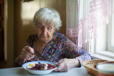 Elderly woman eating soup sitting at a table in the house.