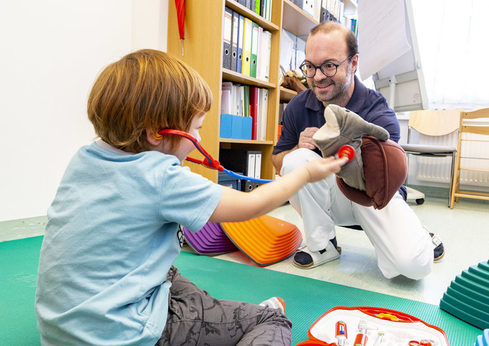 Therapeut spielt mit Patientenkind auf einer Matte.