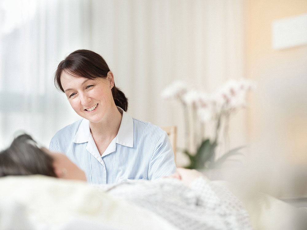 Das Bild zeigt eine weibliche Pflegeperson  im Gespräch mit einer Patientin.