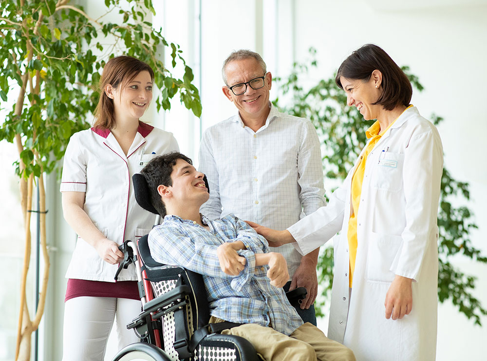 Das Bild zeigt einen Patienten im Rollstuhl mit Mitarbeitenden des Instituts