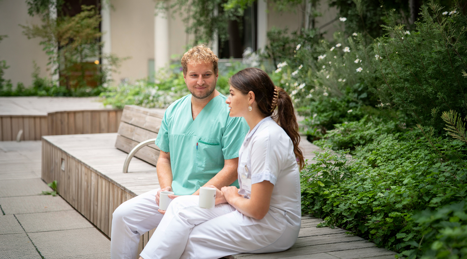 Ein Praxisanleiter und eine Praxisanleiterin, die sich in der Pause im Innenhof des Krankenhauses unterhalten.