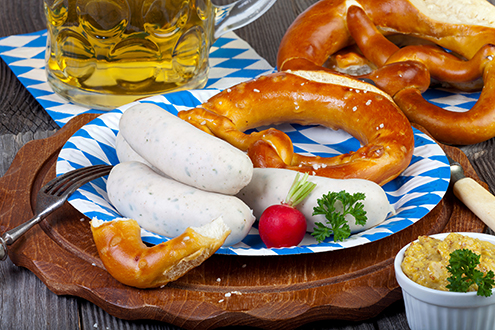 Typisch bayerische Oktoberfest Mahlzeit mit Weißwurst, Senf, Brezeln und einem kühlen Bier auf einem rustikalem Holzti