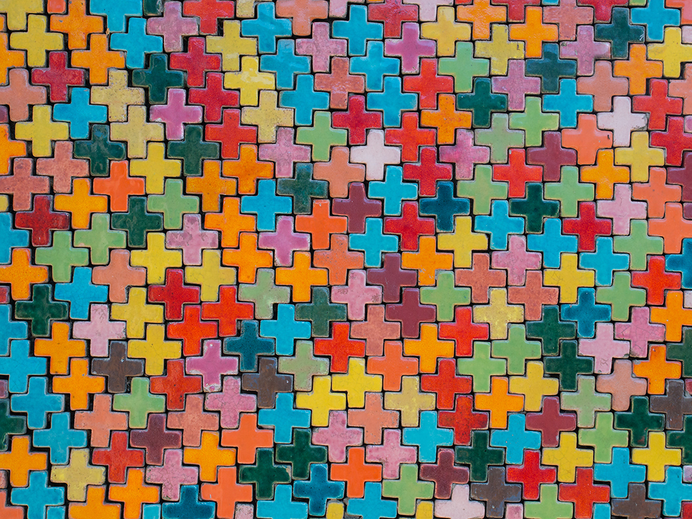 Das Symbolbild zeigt viele kleine, bunte Kreuze in Form eines Puzzles