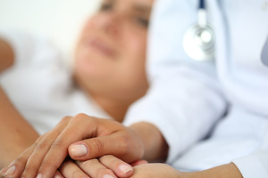 Friendly female doctor hands holding patient hand lying in bed for encouragement, empathy, cheering and support while medical examination. Bad news lessening, compassion, trust and ethics concept