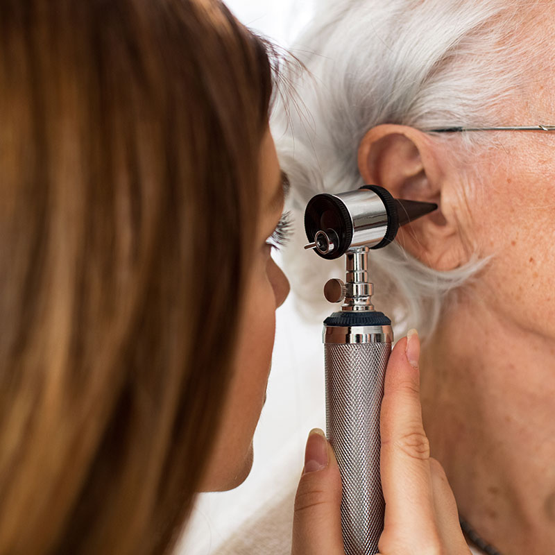 Doctor holding otoscope and examining ear of senior woman in ambulance