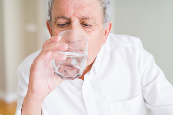 Das Bild zeigt einen Mann, der ein Glas Wasser trinkt.,