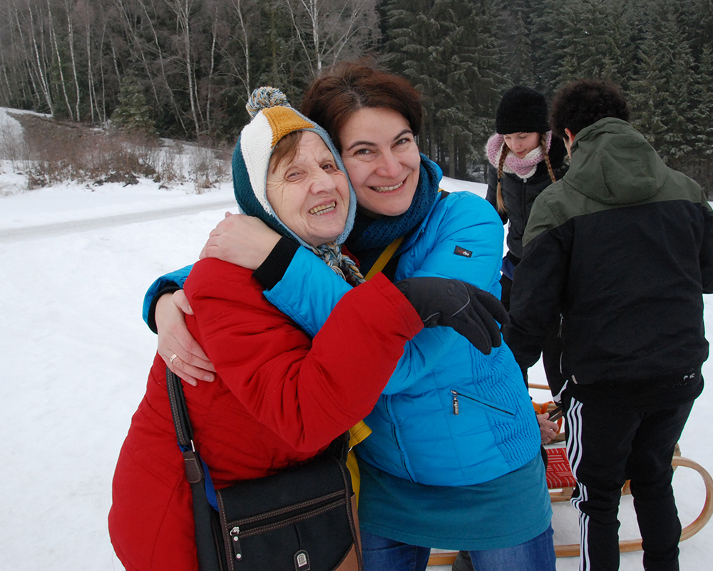 Eine Mitarbeiterin und eine Tageskundin umarmen sich beim Wintersporttag