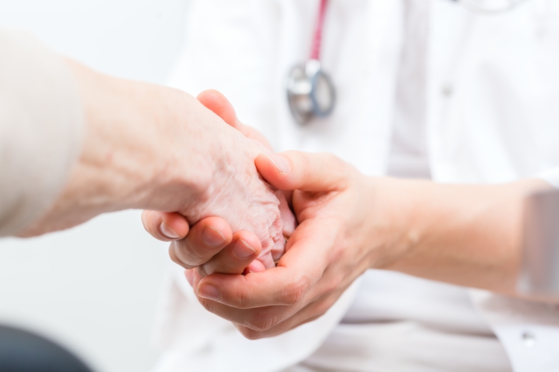 Doctor giving pensioner in surgery comfort and consoling with holding hands 