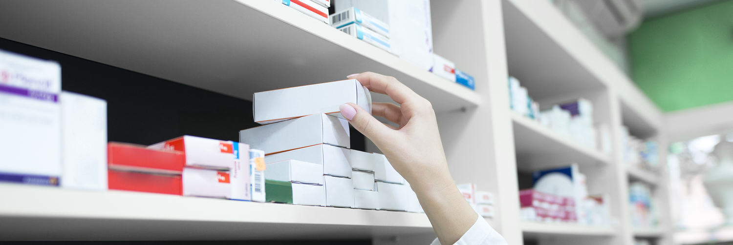 Closeup view of pharmacist hand taking medicine box from the shelf in drug store.