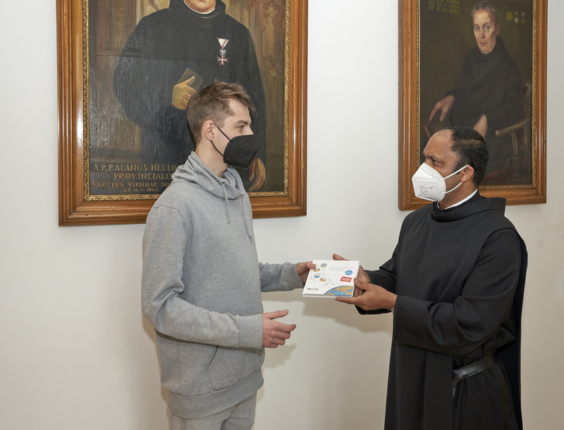 Pater Provinzial Saji Mullankuzhy überreicht in der Wiener Provinzverwaltung der Barmherzigen Brüder ein Exemplar des Buches „Kleine Gase – Große Wirkung: Der Klimawandel“ an einen Mitarbeitenden.