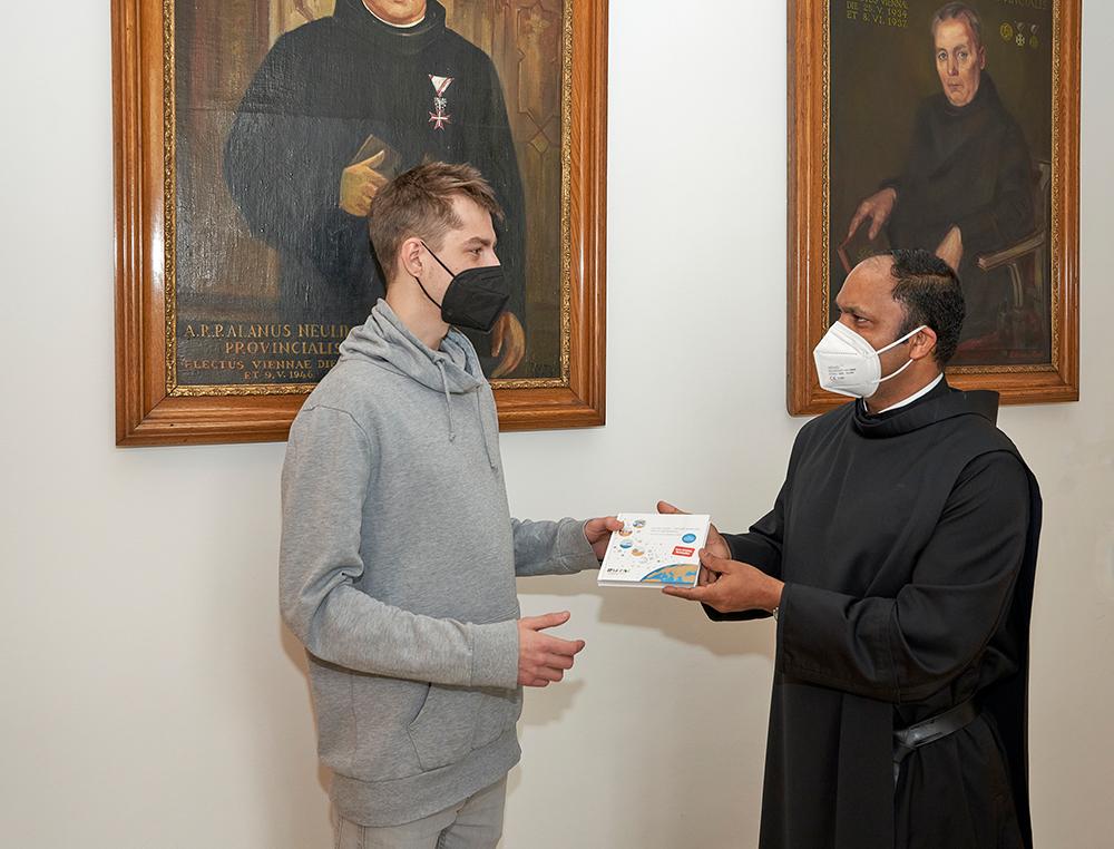 Pater Provinzial Saji Mullankuzhy überreicht in der Wiener Provinzverwaltung der Barmherzigen Brüder ein Exemplar des Buches „Kleine Gase – Große Wirkung: Der Klimawandel“ an einen Mitarbeitenden. / Barmherzige Brüder / Zahrl Pater Provinzial Saji Mullankuzhy überreicht in der Wiener Provinzverwaltung der Barmherzigen Brüder ein Exemplar des Buches „Kleine Gase – Große Wirkung: Der Klimawandel“ an einen Mitarbeitenden.
