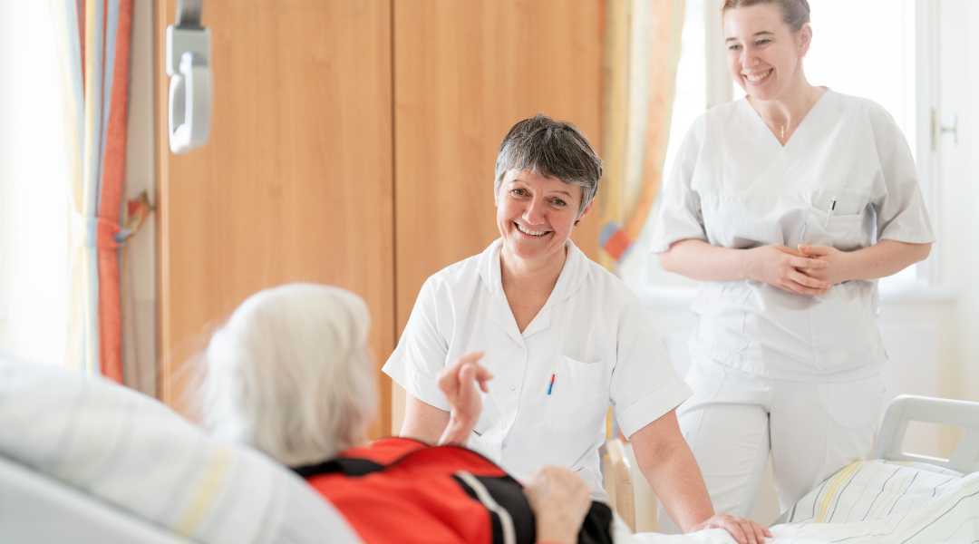 2 Pflegende mit einer Patientin die im Bett liegt