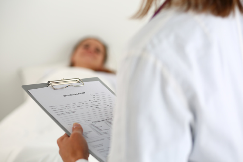 Female medicine doctor filling in patient medical history list during ward round. Medical care or insurance concept. Physician ready to examine patient and help. Patient sleeping