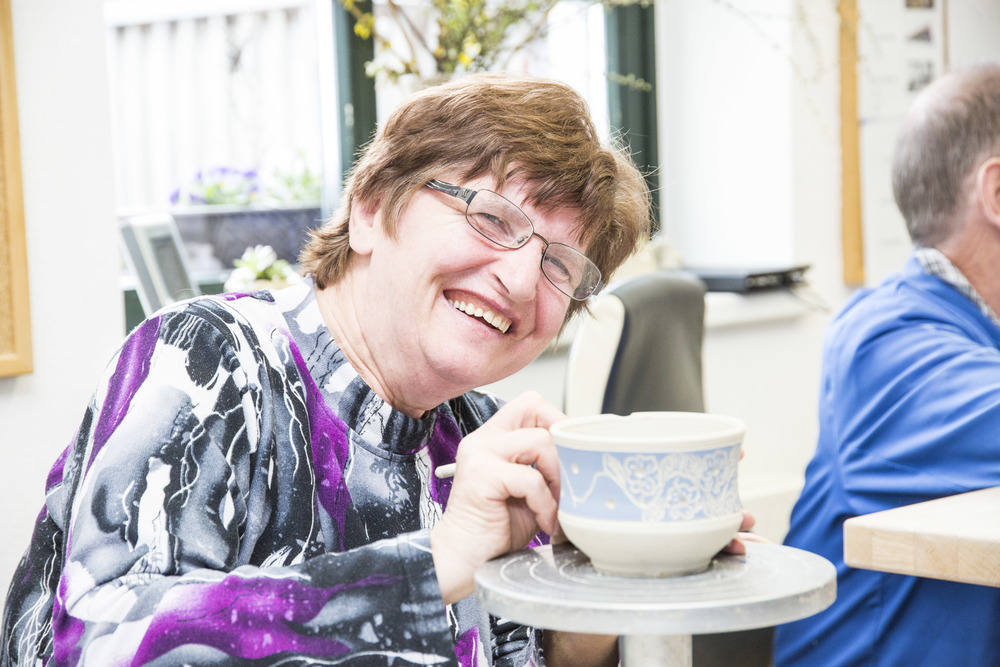Das Foto zeigt eine Bewohnerin der Lebenswelt, die in die Kamera lächelt und gerade eine Keramikschüssel bemalt. 