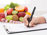 Doctor writing prescription for patient, making diet plan at workplace with fresh fruits, panorama